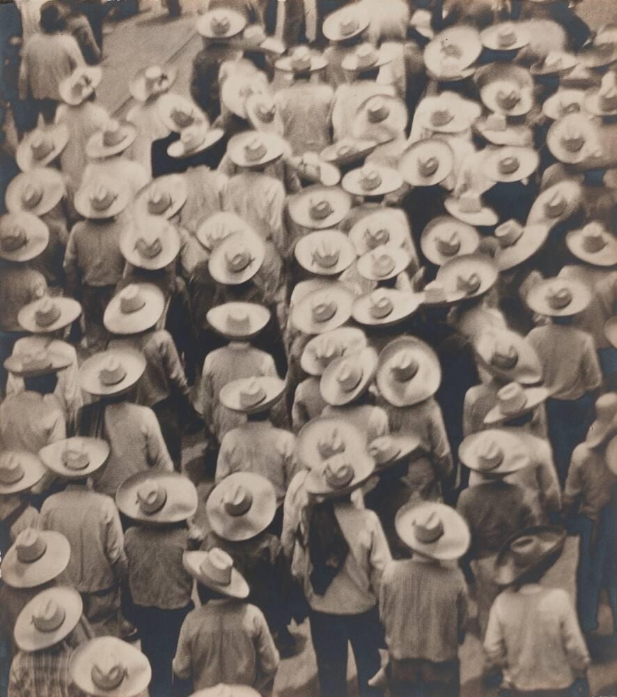 Tina Modotti's 1926 photograph Workers' Parade (Manifestación de Trabajadores), Mexico City. Overhead view of a marching crowd of campesinos and workers in straw hats. Modotti's Mexican-period work led Phillips' April 2026 photographs sale catalogue.