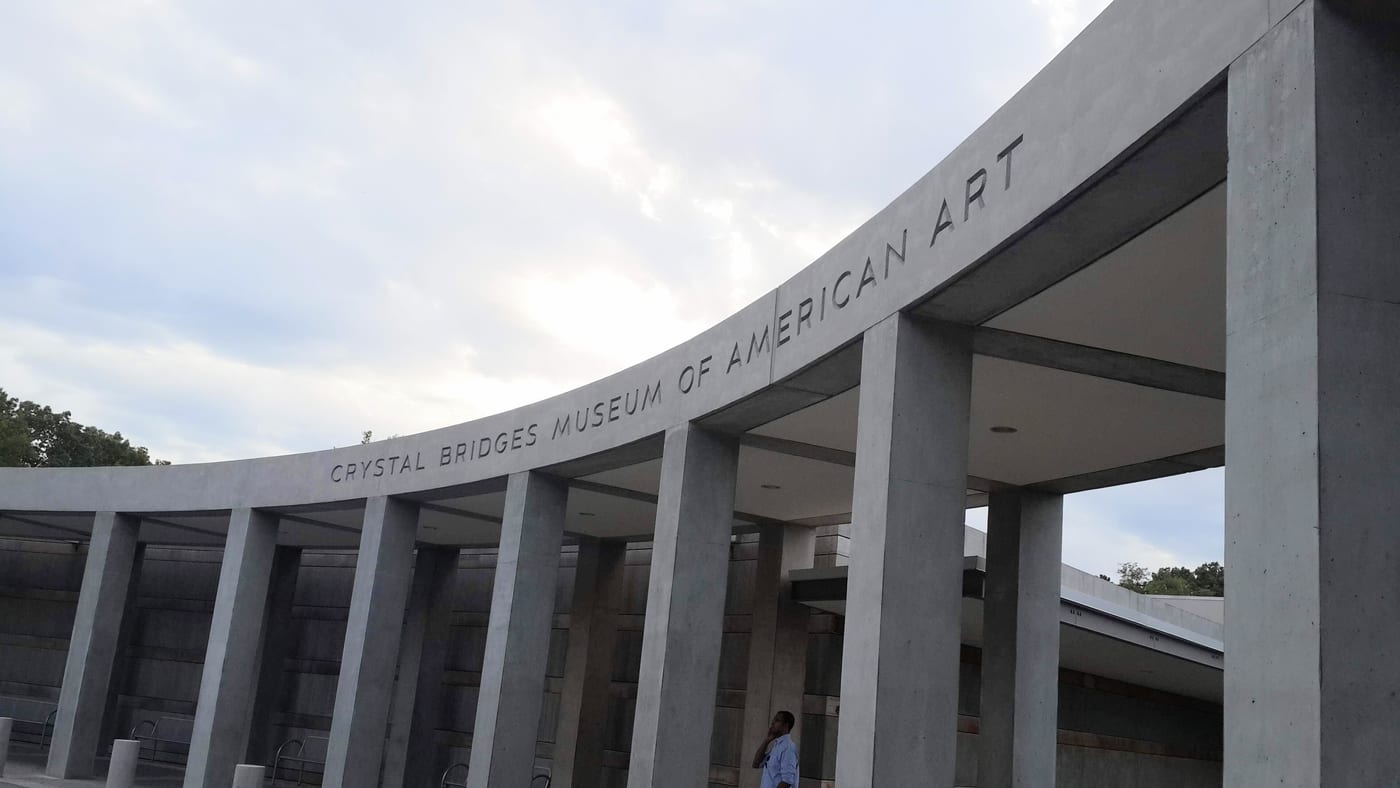 The Crystal Bridges Museum of American Art in Bentonville, Arkansas. Founded by Alice Walton in November 2011 on 120 acres of family-donated land. Moshe Safdie designed the original museum and the 114,000 square foot expansion opening June 2026.